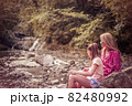 Happy mother with a child sitting on the grass on a background of forested mountains 82480992