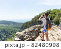 A young girl holds a smartphone to take pictures of a beautiful mountain landscape 82480998