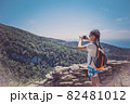 A young girl holds a smartphone to take pictures of a beautiful mountain landscape 82481012