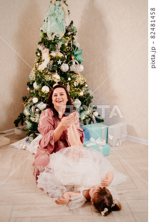 mom plays and holds the legs of her little daughter at the Christmas tree. mom plays and holds the legs of her little daughter at the Christmas tree. 82481458