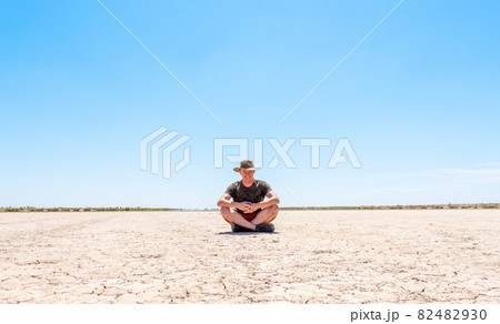 a man with a hat sits on dry, cracked ground 82482930