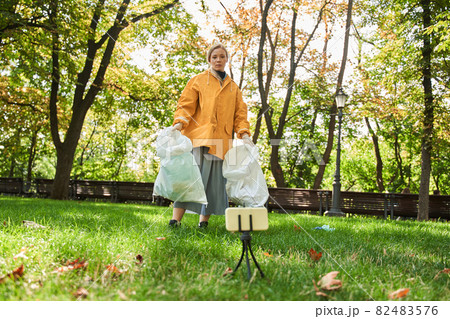 Volunteer woman standing with bag while picking up trash at the park 82483576
