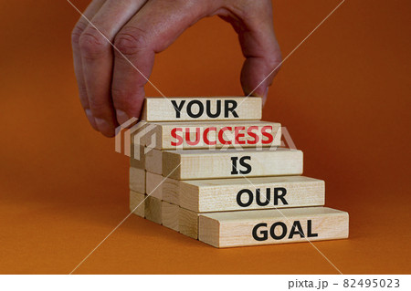 Your success is our goal symbol. Wooden blocks with words 'your success is our goal'. Businessman hand. Beautiful orange background, copy space. Success business goal concept. Your success is our goal symbol. Wooden blocks with words 'your success is our goal'. Businessman hand. Beautiful orange background, copy space. Success business goal concept. 82495023