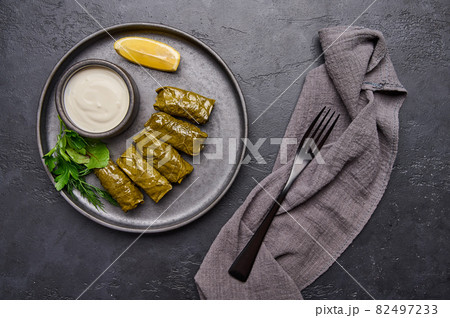 Top view dolma, parsley, saucepan with sour cream and lemon in black plate on dark table Top view dolma, parsley, saucepan with sour cream and lemon in black plate on dark table 82497233