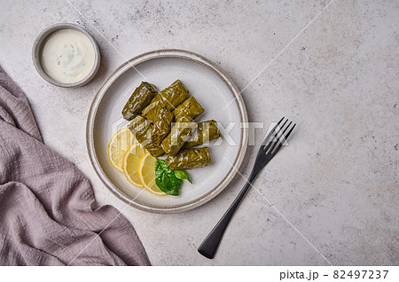 Flat lay dolma, stuffed grape leaves with rice and meat in light plate with with sour cream Flat lay dolma, stuffed grape leaves with rice and meat in light plate with with sour cream 82497237