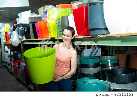 Young woman customer holding big colored plastic pot for garden Young woman customer holding big colored plastic pot for garden 82511153