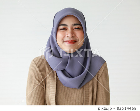 Confident young ethnic woman in Muslim headscarf smiling against white wall Confident young ethnic woman in Muslim headscarf smiling against white wall 82514468