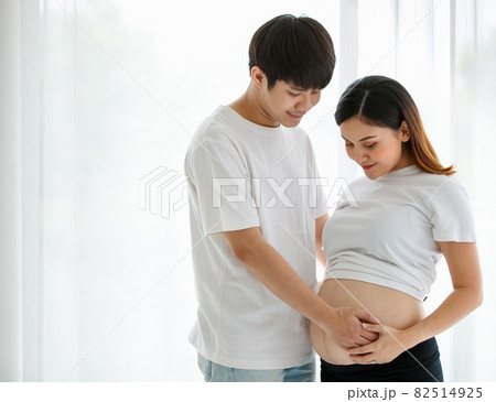 lovely young Asian couple husband and wife standing together smiling and touching a pregnant woman's belly with love and care. Happy and healthy family concept 82514925
