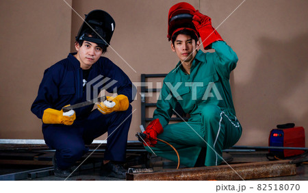young smart Asian sitting and posing to a camera for photographing in a factory. They are wearing a safety outfit for factory working with a mechanic jumpsuit, glove, boots, and welding helmet 82518070