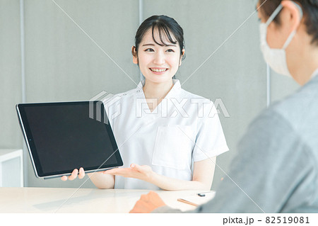 タブレットPCで受付する白衣の女性と患者 タブレットPCで受付する白衣の女性と患者 82519081