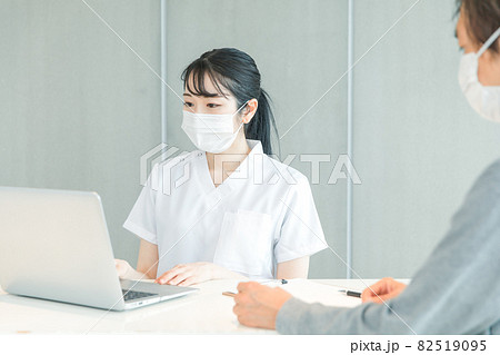 パソコンで受付する白衣の女性と患者 82519095