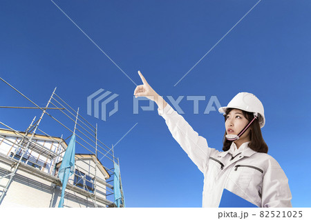 青空と戸建て工事現場を背景に立ち、斜め上を指差し見つめる作業着を着た若い女性 青空と戸建て工事現場を背景に立ち、斜め上を指差し見つめる作業着を着た若い女性 82521025