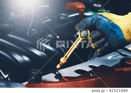 Mechanic hand pulling up oil dipstick of the car engine for checking oil level 82521889