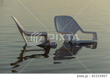 plastic white chairs in the water near the shore on the beach 82524907