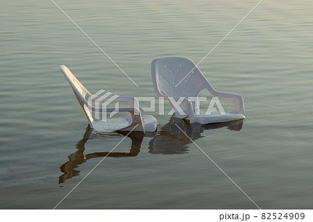 plastic white chairs in the water near the shore on the beach 82524909