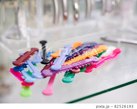 Close up of orthodontic ligature ties for procedure of putting on braces. Multicolored rubber bands or orthodontic O-rings for braces on desk in dental office. Concept of oral medicine. Close up of orthodontic ligature ties for procedure of putting on braces. Multicolored rubber bands or orthodontic O-rings for braces on desk in dental office. Concept of oral medicine. 82526193