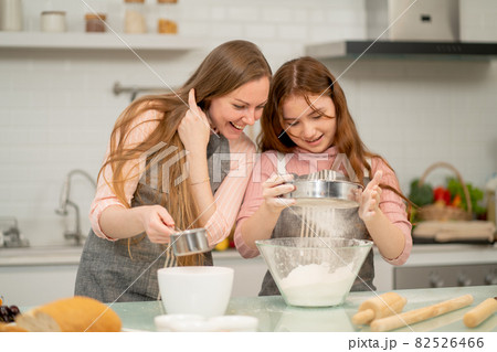 Caucasian mother with apron cheer her daughter to process of cake cooking by sift the flour 82526466