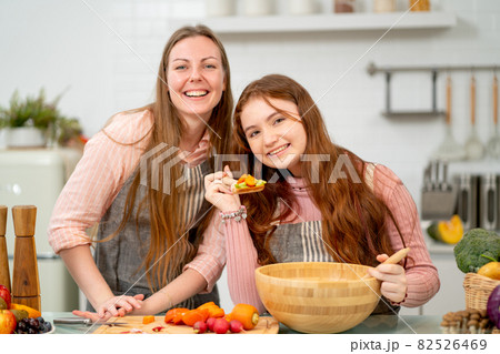 Young daughter hold spoon with mixed vegetable and look at camera with smiling and stay with mother 82526469
