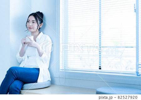 日差しがさしこむリビングでコーヒーを飲みながら寛ぐ女性 82527920