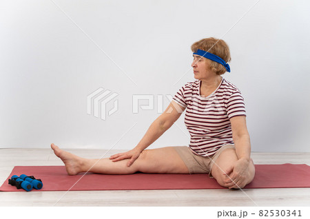 Elderly woman makes bends on a white background. Old lady doing health stretching exercises Elderly woman makes bends on a white background. Old lady doing health stretching exercises 82530341