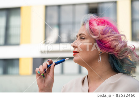 Caucasian woman with colored hair smokes an electronic cigarette. 82532460