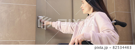 Disabled woman in wheelchair presses call button 82534463
