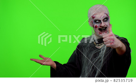 Scary wounded Halloween zombie undead man showing thumbs up and pointing at left on blank space Scary wounded Halloween zombie undead man showing thumbs up and pointing at left on blank space 82535719
