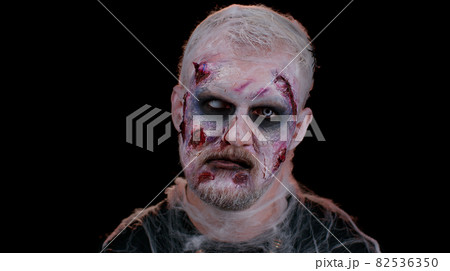 Frightening scary man with Halloween zombie bloody wounded makeup, trying to scare, face expressions 82536350