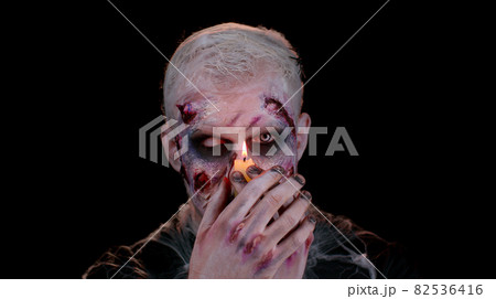 Man with Halloween zombie bloody wounded makeup, trying to scare, spells conjures over a candle Man with Halloween zombie bloody wounded makeup, trying to scare, spells conjures over a candle 82536416