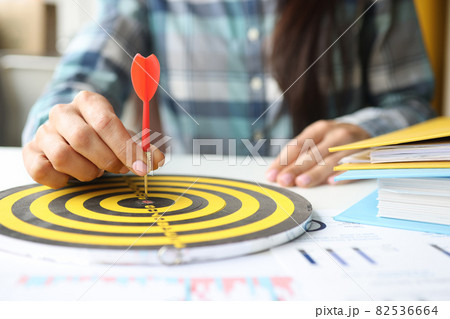 Businesswoman puts dart in center of darts at workplace in office Businesswoman puts dart in center of darts at workplace in office 82536664