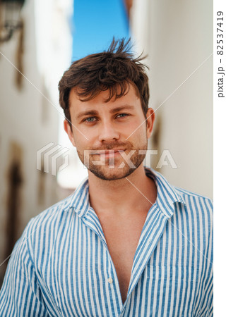 Male tourist in striped shirt looking at camera on blurred background of town street on sunny summer day Male tourist in striped shirt looking at camera on blurred background of town street on sunny summer day 82537419