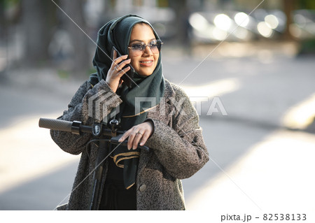Portrait of a muslim girl in a green hijab with a scooter on the street Portrait of a muslim girl in a green hijab with a scooter on the street 82538133