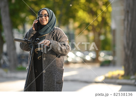 Portrait of a muslim girl in a green hijab with a scooter on the street 82538136