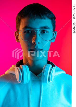 Portrait of young serious boy, student or teen looking at camera isolated on magenta studio backgroud in neon. Human emotions concept. Portrait of young serious boy, student or teen looking at camera isolated on magenta studio backgroud in neon. Human emotions concept. 82539712