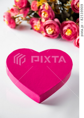Pink heart for valentines day on a background of flowers. Close-up pink heart and a bouquet of flowers on a white background. Place for text, vertical photo. 82539909