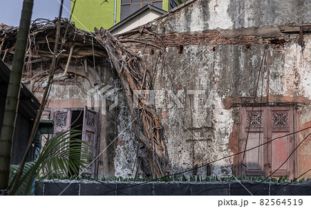 The remains of a derelict abandoned ancient house with antique wooden windows and tree roots growing on the old red brick. The remains of a derelict abandoned ancient house with antique wooden windows and tree roots growing on the old red brick. 82564519