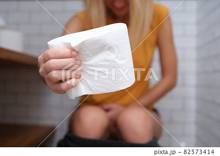 Woman is sitting on t toilet and holding roll of toilet paper Woman is sitting on t toilet and holding roll of toilet paper 82573414