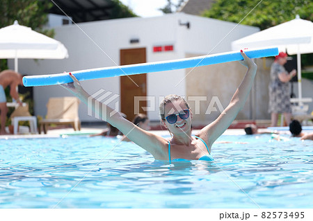 Young woman in sunglasses is engaged in aqua aerobics in outdoor pool Young woman in sunglasses is engaged in aqua aerobics in outdoor pool 82573495