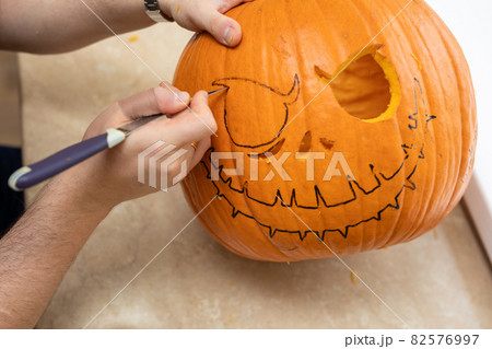 Human hands making face of Halloween pumpkin with knife. Process of making jack-o-lantern at home. Human hands making face of Halloween pumpkin with knife. Process of making jack-o-lantern at home. 82576997