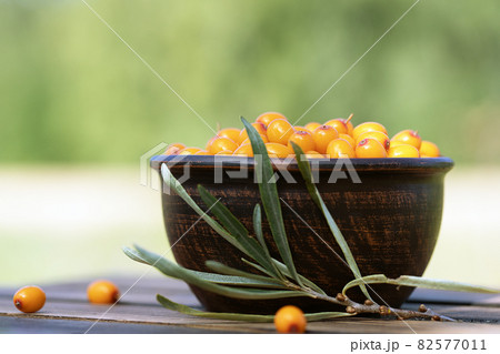 sea buckthorn berries in ceramic bowl on wooden table in garden 82577011