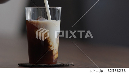 pour milk into ice coffee on black walnut table pour milk into ice coffee on black walnut table 82588238