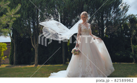 A young bride is standing in a park and her veil is slowly falling her veil is slowly falling 82589962