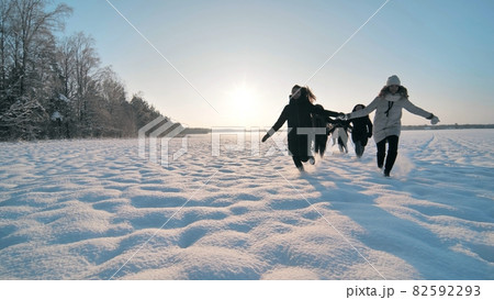 Cheerful girls run hand in hand across a snowy field. 82592293