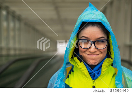 Smiling young woman in a jacket and raincoat on a travolator. Girl in protective clothing from the rain Smiling young woman in a jacket and raincoat on a travolator. Girl in protective clothing from the rain 82596449