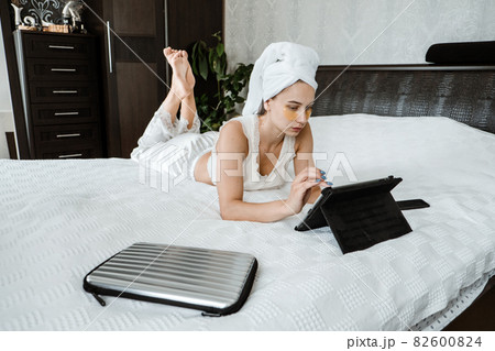 Work from home, freelance at home, remote work, e-learning, online education. Happy stylish young woman in pajamas sitting on white bed with tablet 82600824