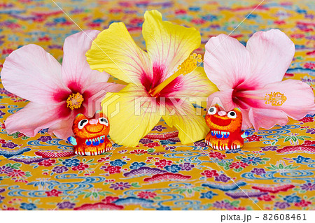 ミンサー織の上に乗るハイビスカスとシーサー 82608461