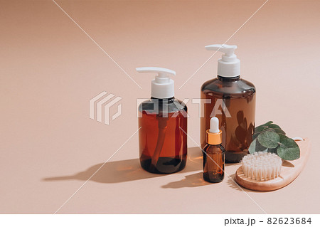Set of natural bathroom amenities - glass dropper bottles with natural organic cosmetics, natural face or body dry brush, eucalyptus oil, cream, lotion, essential oils on brown background. Mockup 82623684