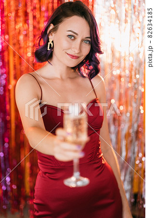 Christmas party. Festive woman. Holiday toast. Elegant happy lady purple curly hair cheering glass champagne on shimmering golden red cascade curtain decoration background blur light. Christmas party. Festive woman. Holiday toast. Elegant happy lady purple curly hair cheering glass champagne on shimmering golden red cascade curtain decoration background blur light. 82634185