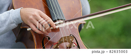 Photography of a street musician plays the cello on a city street on a spring day. Frontal view. Festive mood. Street concert. Closeup photography Photography of a street musician plays the cello on a city street on a spring day. Frontal view. Festive mood. Street concert. Closeup photography 82635003