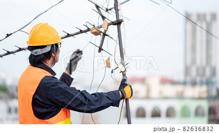 Asian worker repairing an old TV antenna on rooftop 82636832